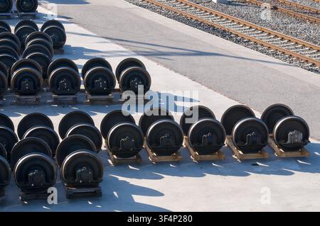 Hohe Blickwinkelaufnahme mehrerer schwerer Stahl-Zugradsätze mit Achsen, die ordentlich auf Holzunterstützungen in einem Außenlager neben dem Bahngleis angeordnet sind Stockfoto