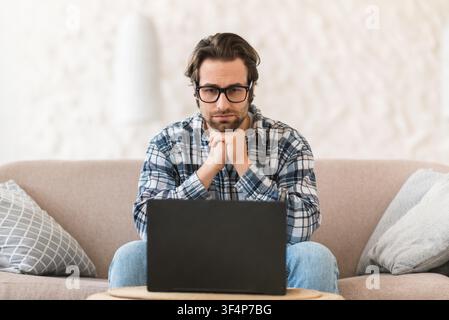 Konzentrierter kaukasischer Mann arbeitet an einem Laptop zu Hause, Freizeitkleidung, Home-Office-Konzept Stockfoto