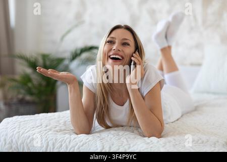 Glückliche Frau telefoniert im Bett in einem gemütlichen Schlafzimmer, entspannter Lebensstil Stockfoto