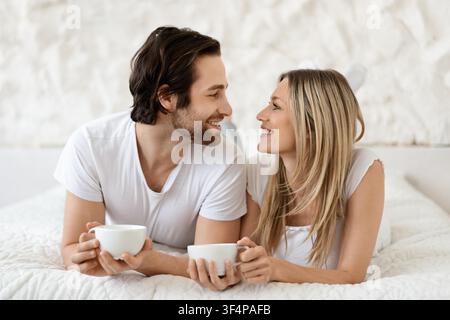 Glückliches Paar genießt Kaffee zusammen mit Lächeln im modernen Schlafzimmer, Lebensstilkonzept Stockfoto