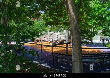 Eine rustikale Holzstamm-Kletterstruktur steht auf farbenfrohem Gummi-Sicherheitsbelag in einem schattigen städtischen Park-Spielplatz. Stockfoto