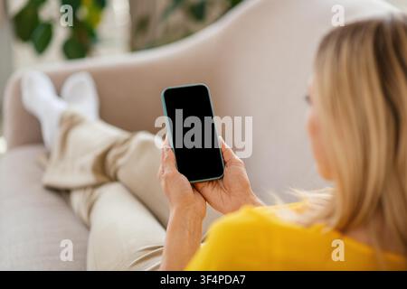 Unerkennbare Frau verwendet Smartphone, während sie zu Hause auf dem Sofa entspannt, Technologie-Konzept Stockfoto