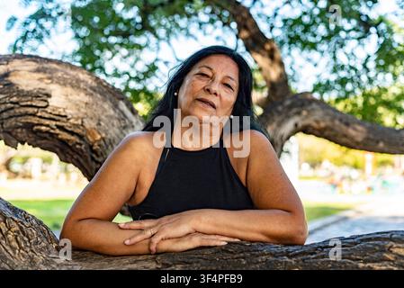 Sanfter Blick einer reifen südamerikanischen Frau, die sich bequem gegen einen großen alten Baum lehnt Stockfoto
