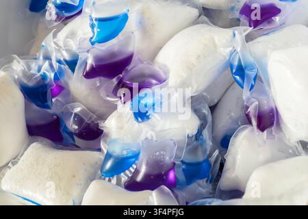 Eine Nahaufnahme aus hohem Winkel eines unordentlichen Haufens von Mehrkammer-Geschirrspülmittel-Pads. Das Bild zeigt lösliche Plastikkapseln, die blaues und pu Stockfoto