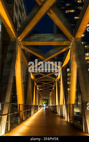 New York, NY - USA - 20. Jul 2026 Beleuchtete Stahl-Fußgängerbrücke bei Nacht in Hudson Yards, New York City, die geometrische Symmetrie und warmes Licht zeigt Stockfoto