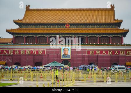 Peking, China – 27. August 2017: Eine große rote Backsteinstruktur mit einem auffälligen Porträt von Mao Zedong hängt über einer Menge, die Schirme hält, umgeben Stockfoto