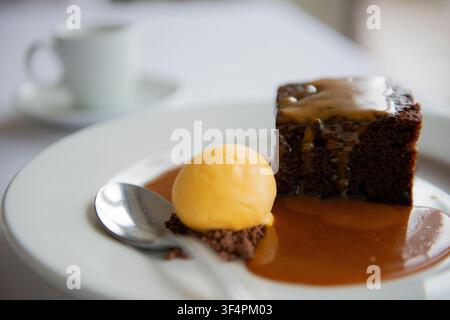 Eine verlockende Kuchenplatte, die mit süßer Sauce beträufelt ist, gepaart mit cremigem Eis auf einem weißen Teller. Stockfoto