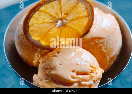 Eine Schüssel mit Löffeln orangefarbenen Eiscremes, garniert mit einer einzigen Scheibe getrockneter Orange Stockfoto