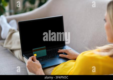 Unerkennbare Frau verwendet einen Laptop und hält eine Kreditkarte zu Hause, Online-Shopping-Konzept Stockfoto