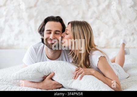 Glückliches junges Paar, das im Bett lächelt und sich küsst, entspannt zu Hause. Lifestyle-Konzept Stockfoto
