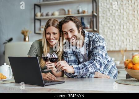 Glückliches junges Paar stößt mit Rotwein in der Küche an und genießt gemeinsame Qualitätszeit Stockfoto