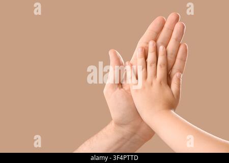 Erwachsenenhand, die eine Kinderhand hält, Konzept für familiäre Unterstützung und Fürsorge, Schutz und Sicherheit, isoliert auf einem braunen Hintergrund Stockfoto