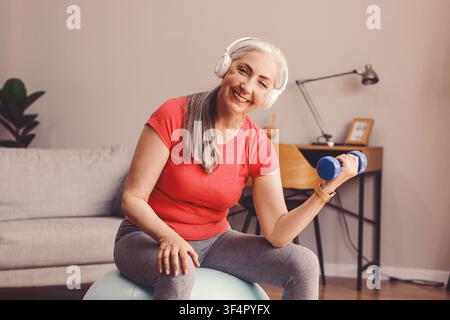 Lächelnde ältere kaukasische Frau, die mit einem Hantelstab trainiert, Fitnesskonzept zu Hause Stockfoto