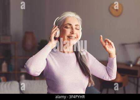 Glückliche ältere kaukasische Frau genießt Musik mit Kopfhörern zu Hause, entspannt Stockfoto