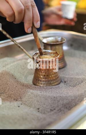 Eine Person rührt Türkischen Kaffee in einem Topf, während dieser im warmen Sand steht.. Stockfoto