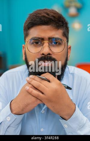 Der indische Mann zu Hause hält Stift für Gesicht und blickt vorsichtig nach vorne, um Aufgaben mit konzentriertem Verstand zu planen. Ein Araber aus der Nähe denkt über Ziele nach, die sich durch die nächsten Schritte und strategischen Ideen drehen Stockfoto