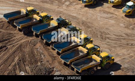 Birmingham, England, Vereinigtes Königreich - 12. Juli 2026: Luftaufnahme einer Reihe gelber gelenkter Kipper, die auf einer schlammigen Baustelle geparkt sind. Stockfoto
