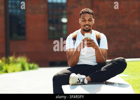 Lächelnder schwarzer Mann im Freien, der ein Smartphone verwendet, entspannte Atmosphäre Stockfoto