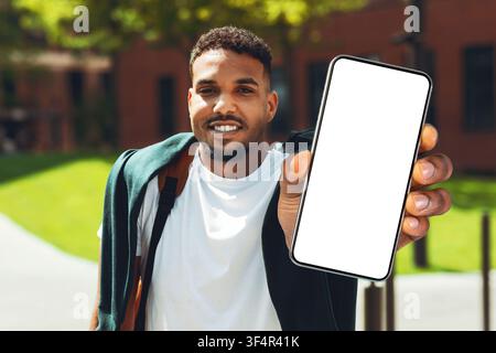 Lächelnder schwarzer Mann zeigt Smartphone mit leerem Bildschirm im Freien, Mockup-Konzept Stockfoto