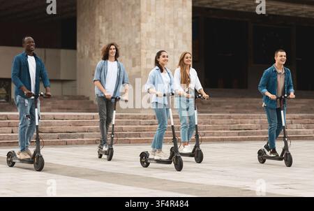 Gruppe junger Erwachsener fährt gemeinsam auf Elektroscootern in der Stadt, lächelnd, lustiger Lebensstil Stockfoto