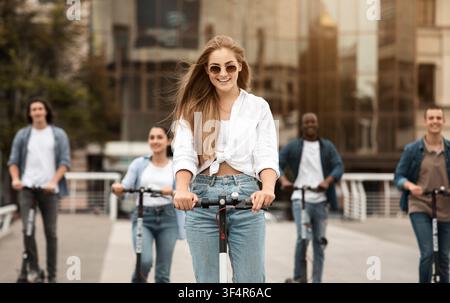 Glückliche junge Frau fährt mit Freunden E-Scooter, städtische Umgebung, Konzept für Outdoor-Aktivitäten Stockfoto