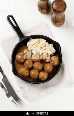 Oberansicht schwedischer Fleischbällchen mit Kartoffelpüree. Traditionelles skandinavisches Gericht in einer schwarzen Gusseisenpfanne auf einem weißen Küchentisch Stockfoto