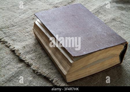 Ein altes Buch vor einem Hintergrund aus rauer Stoff. Ein Buch mit vergilbten Seiten in einem braunen Ledereinband. Stockfoto