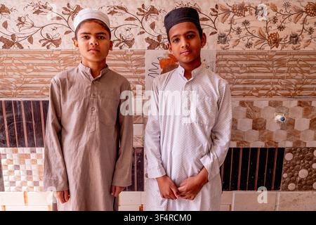Zwei Jungen in Kurta und Taqiyah stehen vor einer Wand mit Blumenmustern und dekorativen Fliesen in der Jama Masjid Khairuddin Grand Moschee Stockfoto