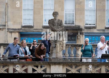 Bath, UK - 25. Jun 25: Touristen versammeln sich neben einer klassischen Statue auf der Terrasse mit Blick auf die Römischen Bäder in Bath, England. Stockfoto