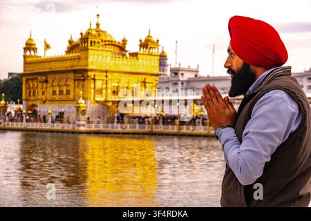 Ein Sikh betet vor dem Goldenen Tempel, der in goldenem Licht gebadet und im Wasser gespiegelt ist, in Amritsar, Indien. Stockfoto