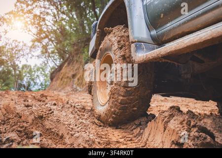 Geländewagen mit Allradantrieb und schlammbedecktem Reifen auf einer roten Schotterstraße durch den Wald, fängt Abenteuerfahrten, schlammige Pfade, Überlandreisen und raues Gelände ein Stockfoto