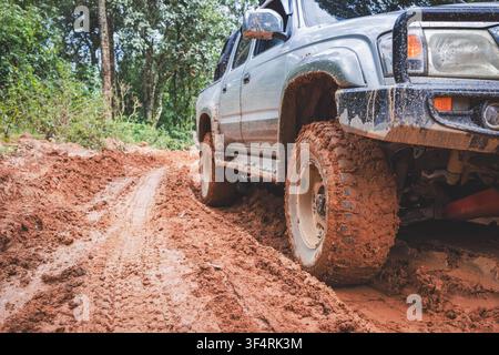 Nahaufnahme eines schlammbedeckten Rads an einem Geländewagen, der einen roten Lehmpfad im Wald entlangfährt, zeigt Offroad-Abenteuer, schlammige Straße, Überlandreise, a Stockfoto