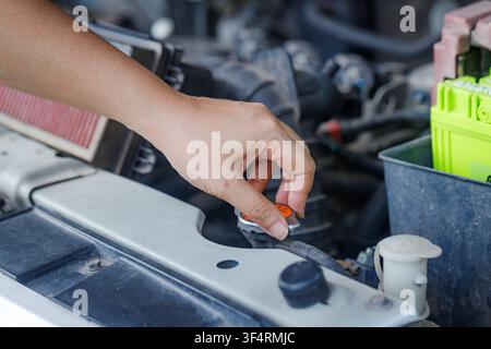 Nahaufnahme einer Hand einer Frau, die den Motoröldeckel öffnet, um den Ölstand zu prüfen, was die Fahrzeugwartung und Motorpflege in einer Werkstattsumgebung hervorhebt Stockfoto