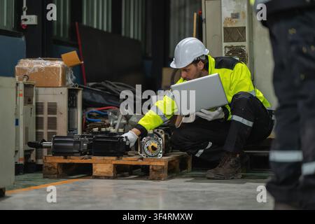 Industrieingenieure mit Laptop in der Hocke, die Maschinenteile Servomotorenteile eines Roboterarms auf einer Palette in der Fabrik inspizieren. Konzept des Lagerkontrolls Stockfoto