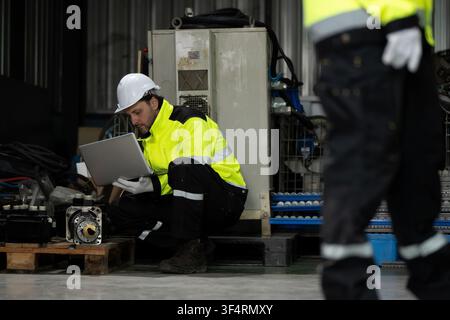 Industrieingenieure mit Laptop in der Hocke, die Maschinenteile Servomotorenteile eines Roboterarms auf einer Palette in der Fabrik inspizieren. Konzept des Lagerkontrolls Stockfoto