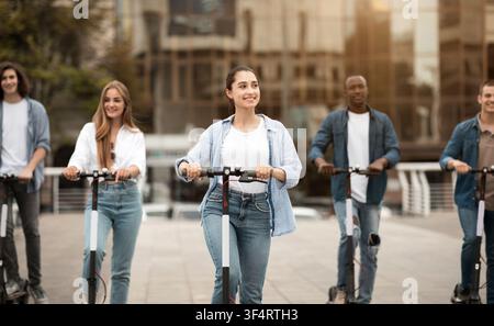 Gruppe von jungen Erwachsenen auf Elektroscootern in der Stadt, glückliche lächelnde Menschen, urbaner Lebensstil Stockfoto