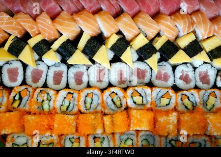 Eine farbenfrohe Auswahl an verschiedenen Sushi- und Maki-Sorten, darunter Lachs- und Thunfisch-Nigiri, Fischrogenröllchen und Kreationen, die mit frischem Gemüse garniert sind, alles bea Stockfoto