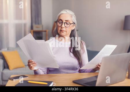 Seniorin prüft Dokumente im Home Office, konzentriert und engagiert, Geschäftskonzept Stockfoto