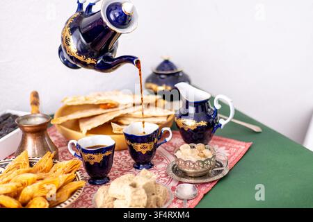 Kobaltblauer Vintage-Dekanter-Krug-Getränk in der Tasse. Süßigkeiten auf dem Tisch Honig-Baklava und Halva auf einer gemusterten roten Tischdecke. Stockfoto