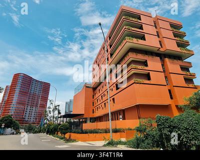 Niedrigwinkelaufnahme eines lebendigen orangefarbenen zeitgenössischen Wohnhauses mit üppigen vertikalen Gärten auf Balkonen vor einem klaren blauen Himmel in einer städtischen Umgebung Stockfoto