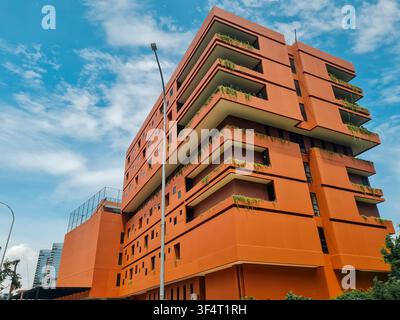 Niedrigwinkelansicht eines lebhaften orangefarbenen Wohngebäudes mit nachhaltigen grünen Balkonen unter einem blauen Himmel. Stockfoto