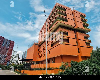Niedrigwinkelaufnahme eines leuchtend orangefarbenen Gebäudes mit vorkragenden Balkonen und üppiger Vegetation vor einem hellen Himmel. Stockfoto