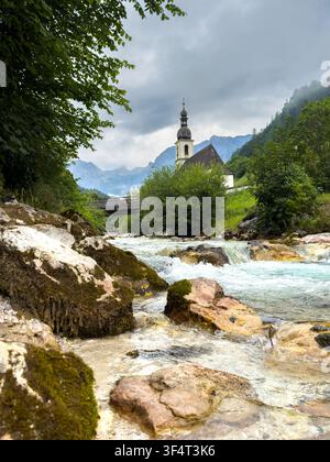 Dorfkirche in Ramsau mit Gebirgsbach in den Berchtesgadener Alpen, Bayern, Deutschland Vertikal Stockfoto
