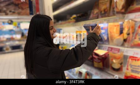 Frau beim Einkauf von Lebensmitteln, die Produkte aus einem gut gefüllten Regal in einem Lebensmittelladen auswählt Stockfoto