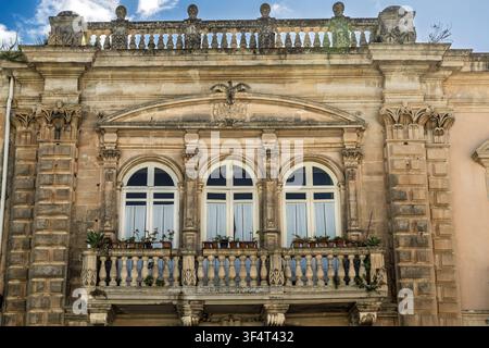 Historische verzierte Steinfaçade & Balkon mit 3 gewölbten Fenstern & Reihen von Topfpflanzen Stockfoto