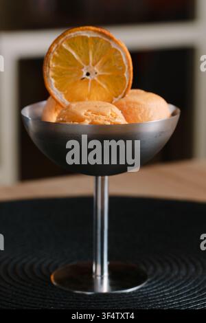 Löffel orangefarbenen Eiscremes, serviert in einer modernen Metallschale, garniert mit einer getrockneten Orangenscheibe Stockfoto