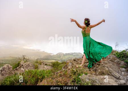 Frau in grünem Kleid, die Freude und Freiheit auf einem nebligen Berggipfel ausdrückt Stockfoto