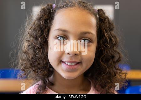 Afroamerikanisches Mädchen lächelt, schaut in die Kamera im Klassenzimmer mit Kreidetafel und blauen Stühlen Stockfoto