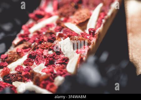 Nahaufnahme einer handgefertigten weißen Kunstschokoladenriegel mit großzügigen Mengen getrockneter Himbeeren und kleinen Stückchen von Nüssen oder anderen Einbänden Stockfoto