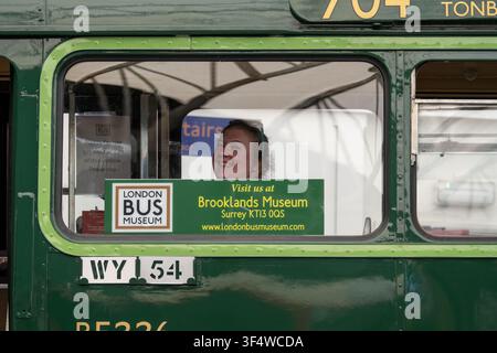 Blick durch das Seitenfenster eines erhaltenen Green-Line-Busses mit einem lächelnden Besucher im Inneren im Brooklands-Museum in Surrey, England. Stockfoto